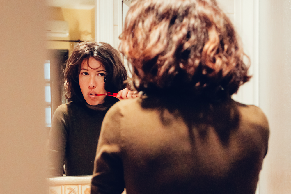 woman brushing her teeth in mirror