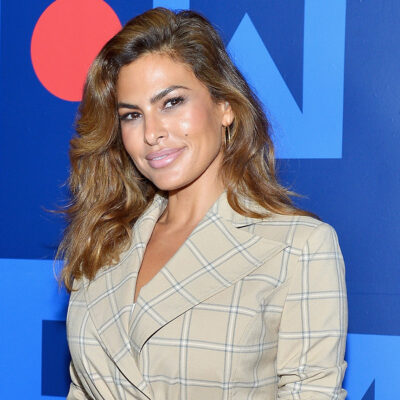Eva Mendes in a beige plaid suit in front of a blue background
