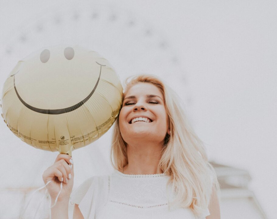 Cheerful woman holding a smiley balloon outdoors on a sunny day, exuding happiness and positivity.